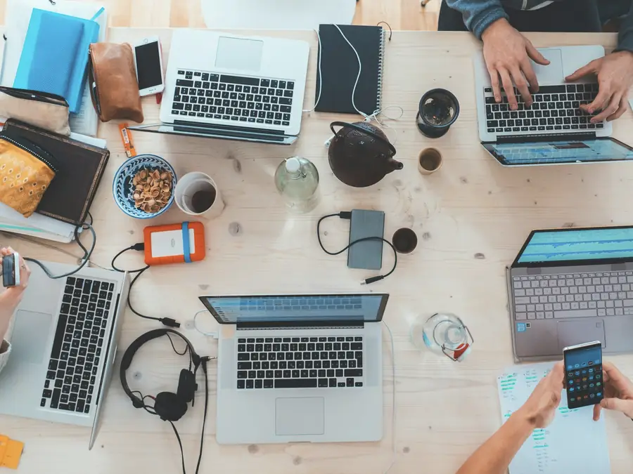 Mesa de trabajo vista desde arriba con portátiles, cuadernos y café